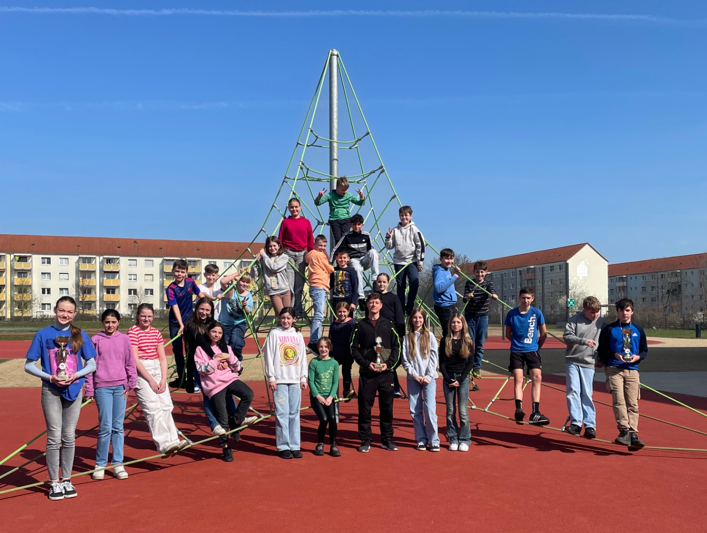Schüler stehen vor Kletterspinne und halten einen Pokal